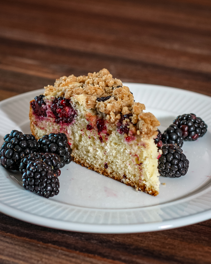blackberry crumb cake on a plate with fresh blackberries