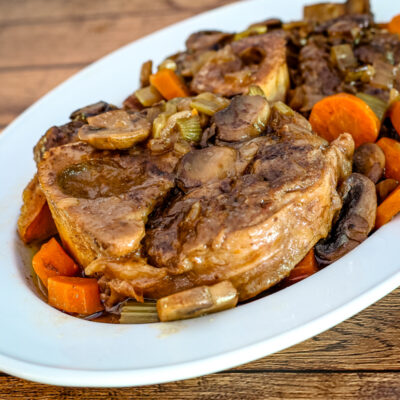 braised beef shanks on a platter with garlic, mushrooms, and carrots