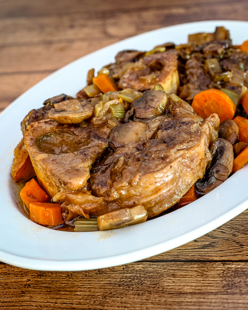 braised beef shanks on a platter with garlic, mushrooms, and carrots