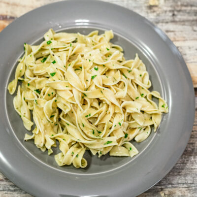 Buttered egg noodles with parsley garnish on a gray plate.