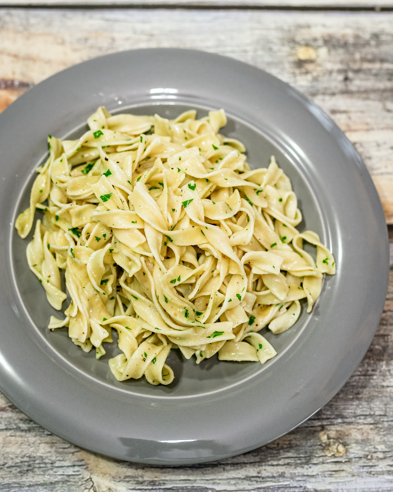 Buttered egg noodles with parsley garnish on a gray plate.