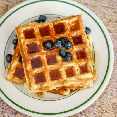 Buttermilk waffles with blueberries and syrup on a vintage restaurant plate.