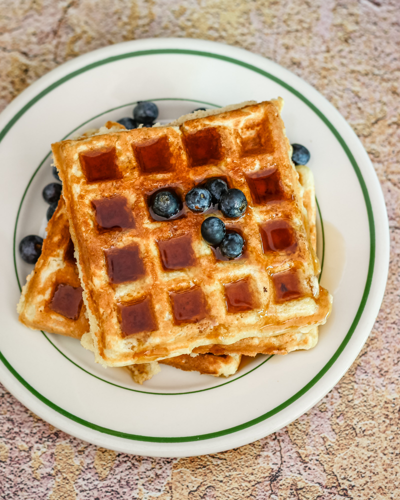 Buttermilk waffles with blueberries and syrup on a vintage restaurant plate.