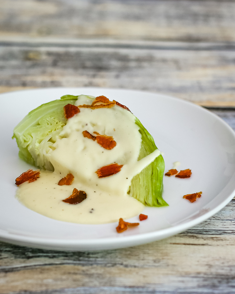 Cabbage wedge on a plate with cheese sauce and crispy bacon.