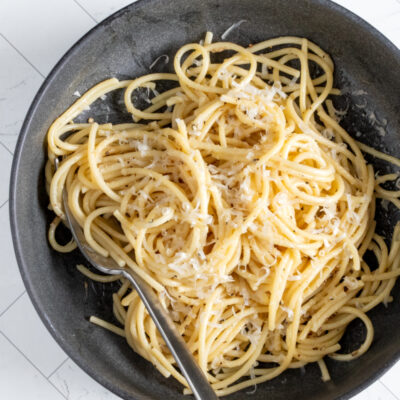 A bowl of cacio e pepe pasta with fresh grated Parmesan cheese and a fork.