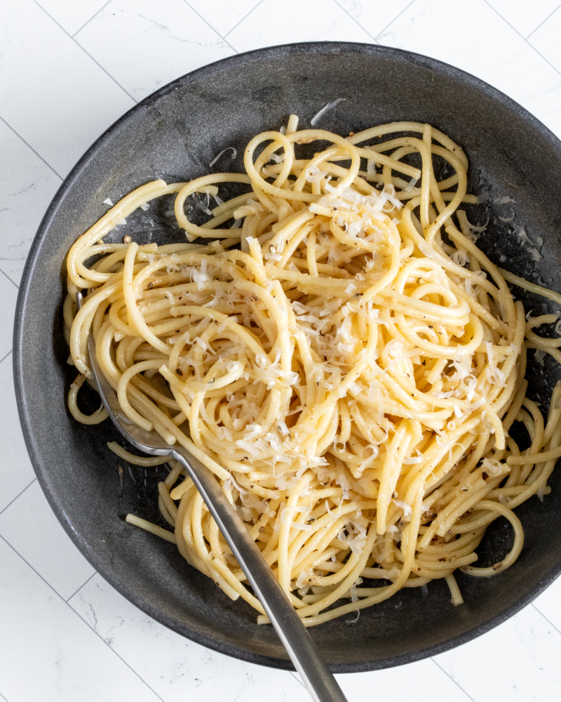 A bowl of cacio e pepe pasta with fresh grated Parmesan cheese and a fork.