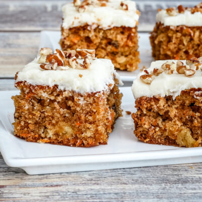 Moist carrot cake squares with cream cheese frosting and chopped nuts on top.