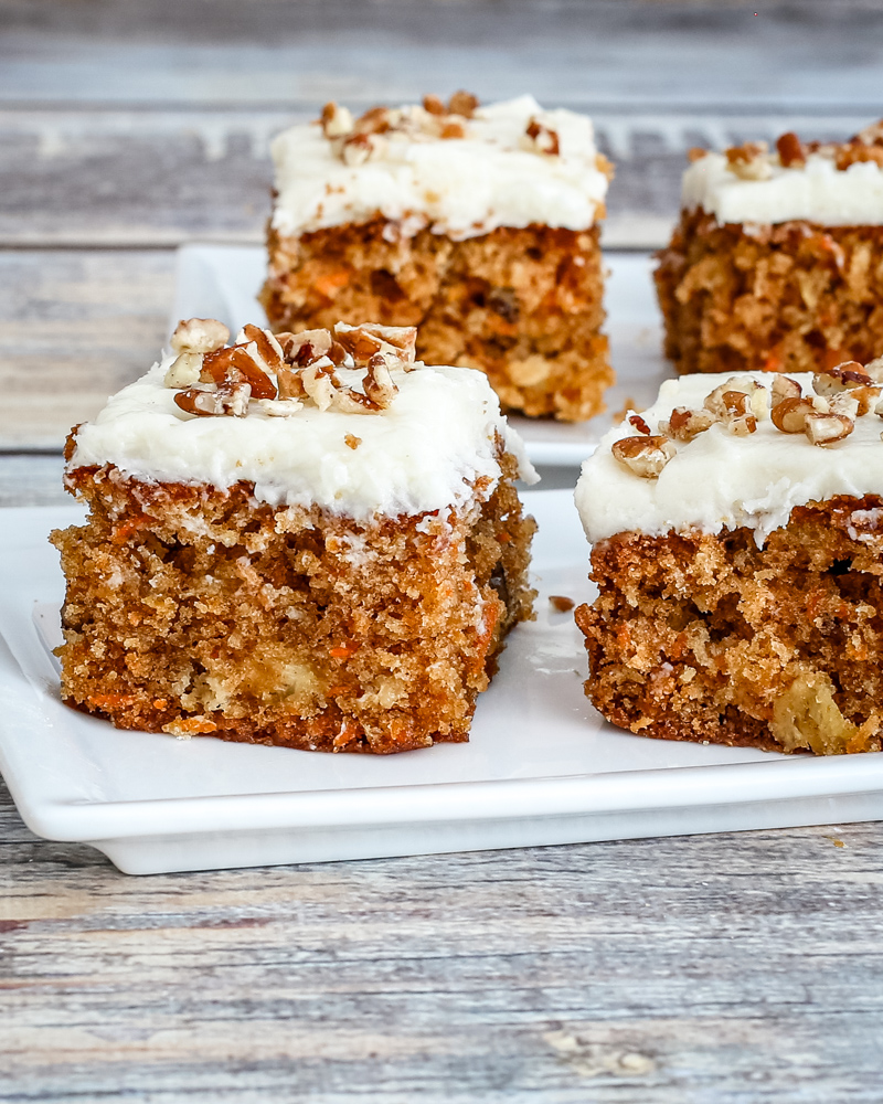 Moist carrot cake squares with cream cheese frosting and chopped nuts on top.