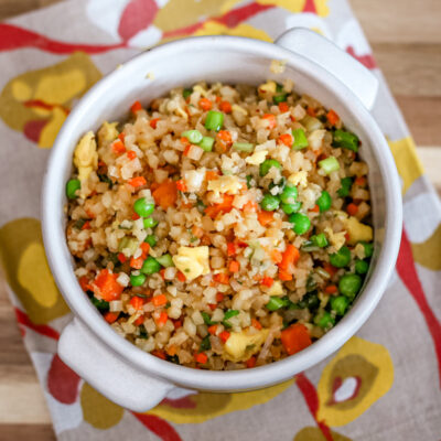 Cauliflower fried rice with mixed vegetables in a white bowl on a colorful cloth.