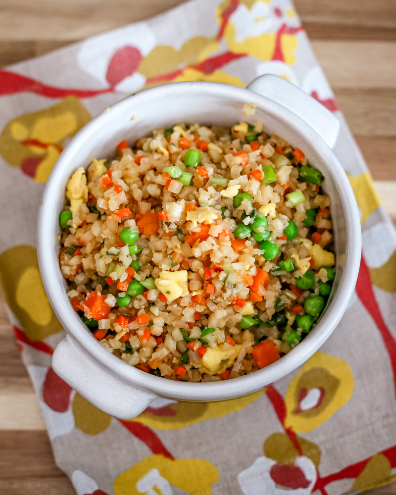 Cauliflower fried rice with mixed vegetables in a white bowl on a colorful cloth.