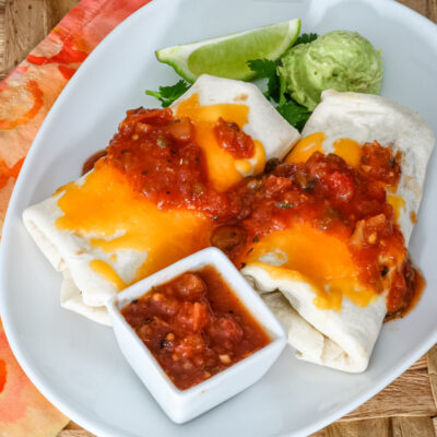 chicken burritos on a plate with salsa and guac