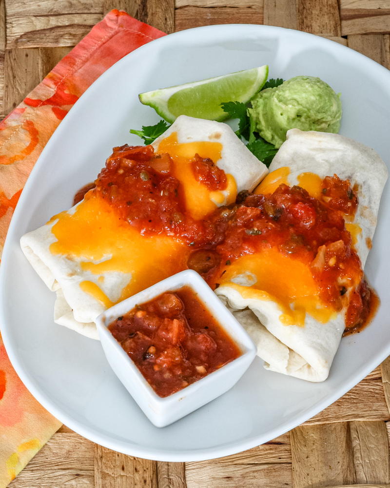 chicken burritos on a plate with salsa and guac