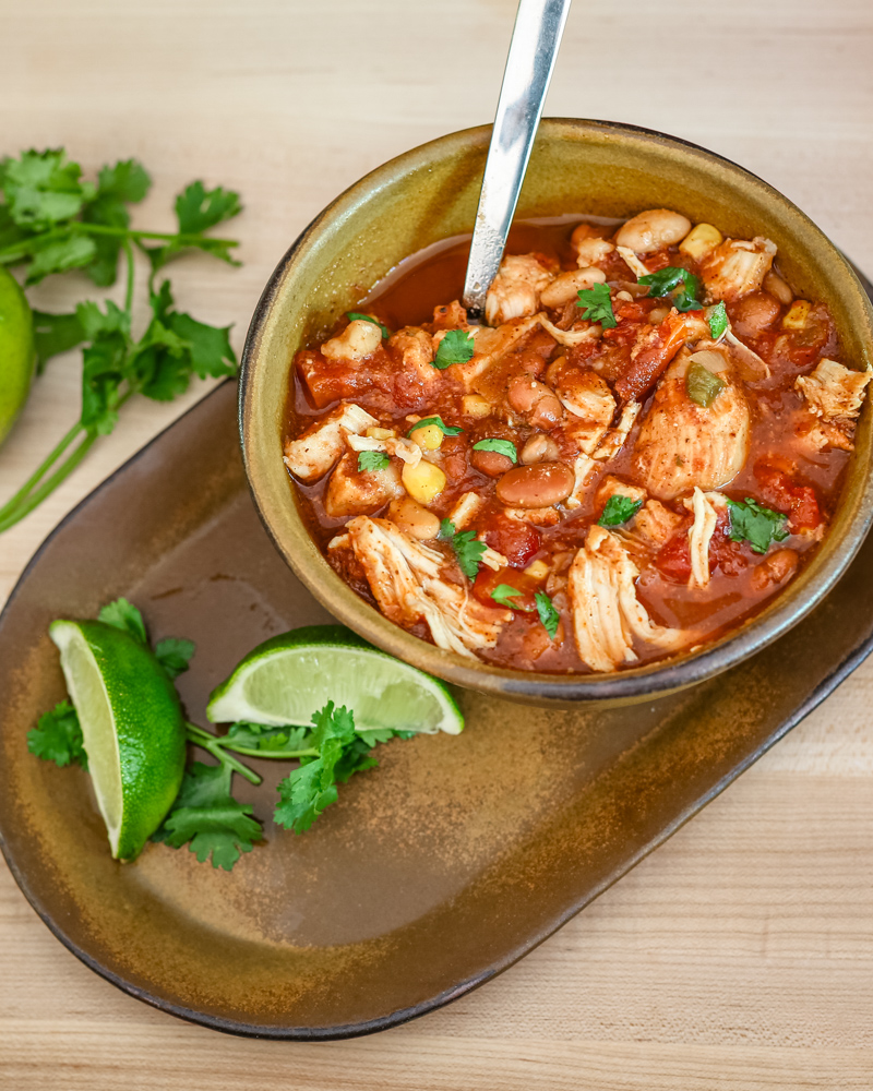 Chicken chili with beans and cilantro garnish in a bowl with some lime wedges.