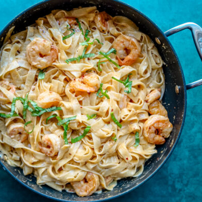 Creamy shrimp pasta in a black skillet with basil garnish.