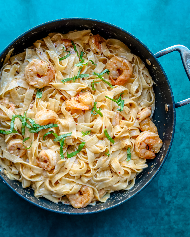 Creamy shrimp pasta in a black skillet with basil garnish.