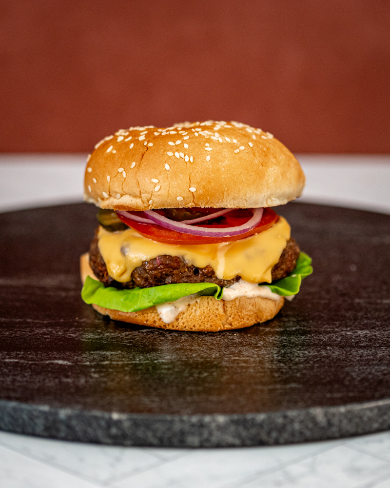 grilled burger with chipotle mayonnaise or aioli on a board with a cheeseburger in the background