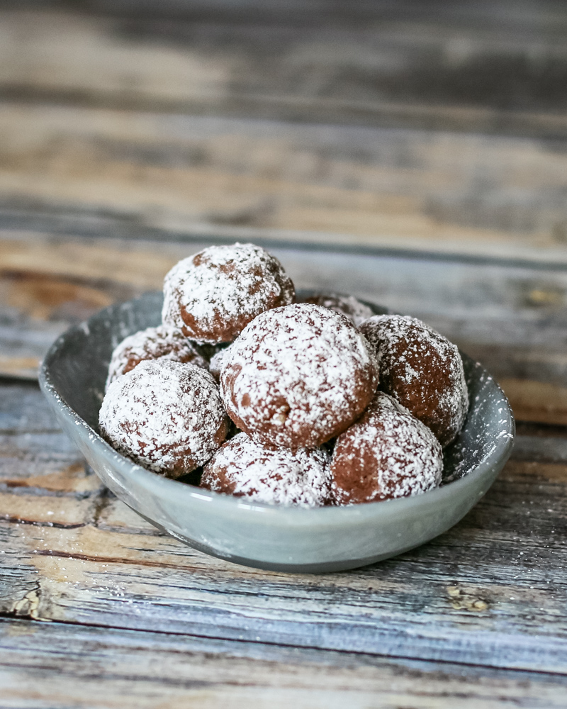 Chocolate butterball cookies stacked in a small dish.