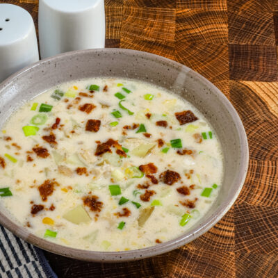 A bowl of clam and corn chowder with green onions and bacon garnish..