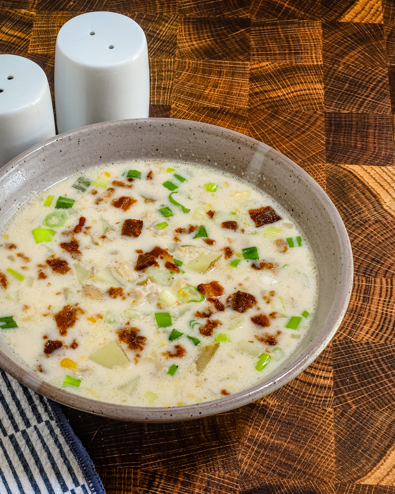 A bowl of clam and corn chowder with green onions and bacon garnish..