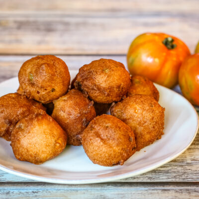 Corn and ham fritters on a white plate with a few tomatoes beside them.