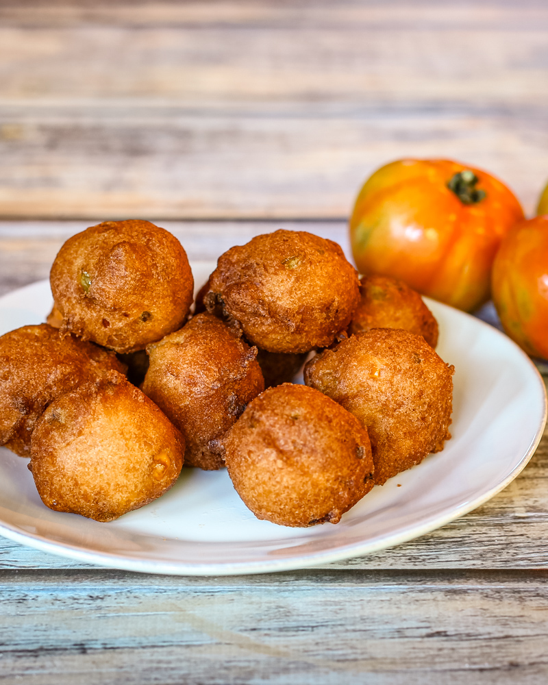 Corn and ham fritters on a white plate with a few tomatoes beside them.