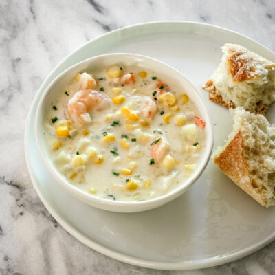 corn and shrimp chowder in a bowl with bread and chives for garnish