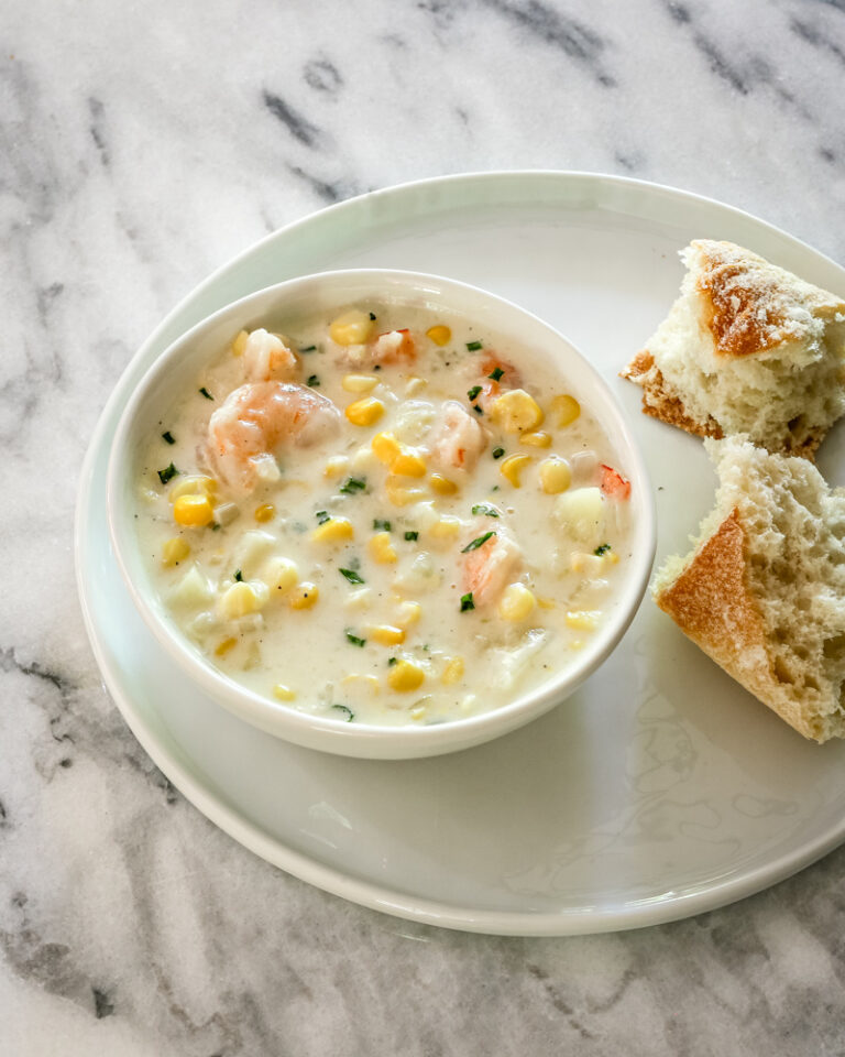 corn and shrimp chowder in a bowl with bread and chives for garnish