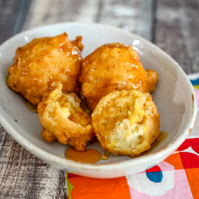 Corn fritters in a small bowl with syrup.