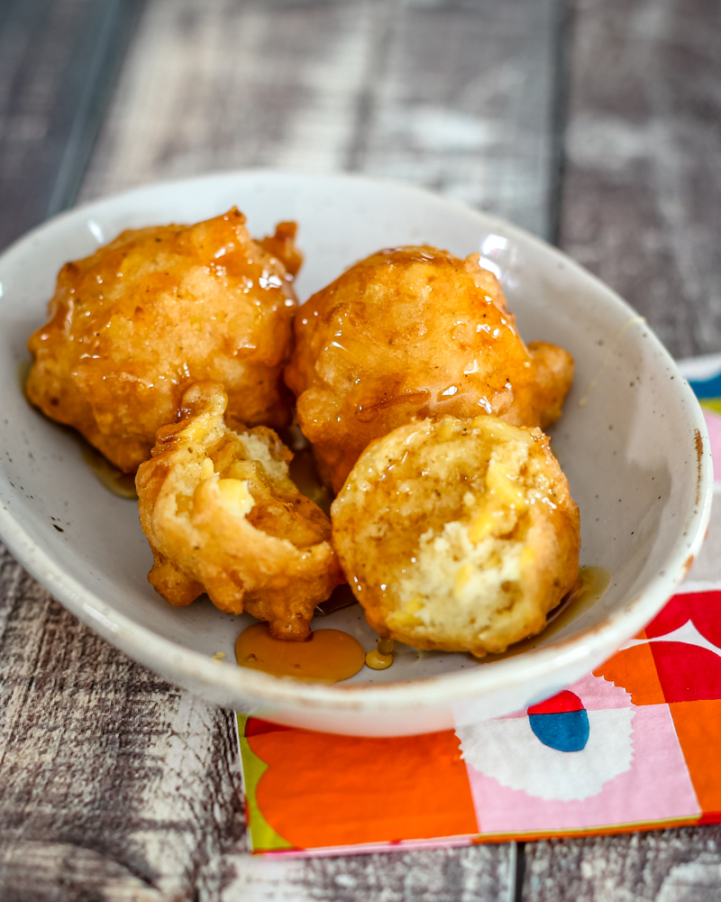 Corn fritters in a small bowl with syrup.