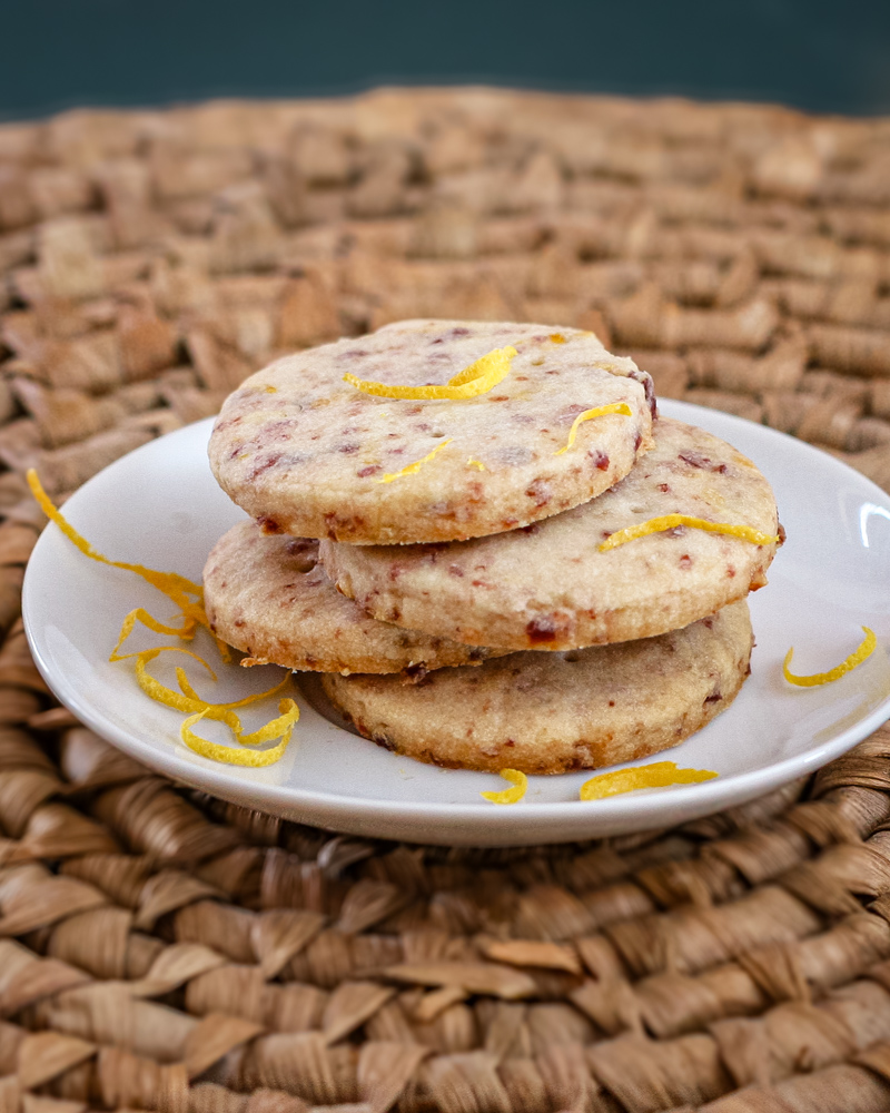 Cranberry orange shortbread cookies on a plate with strips of orange zest.