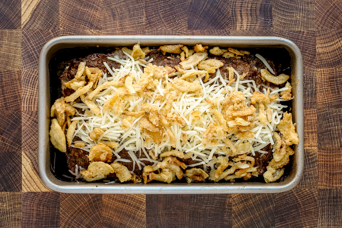 Baked meatloaf with the Gruyere cheese and fried onion rings arranged over the top and ready to go back into the oven.