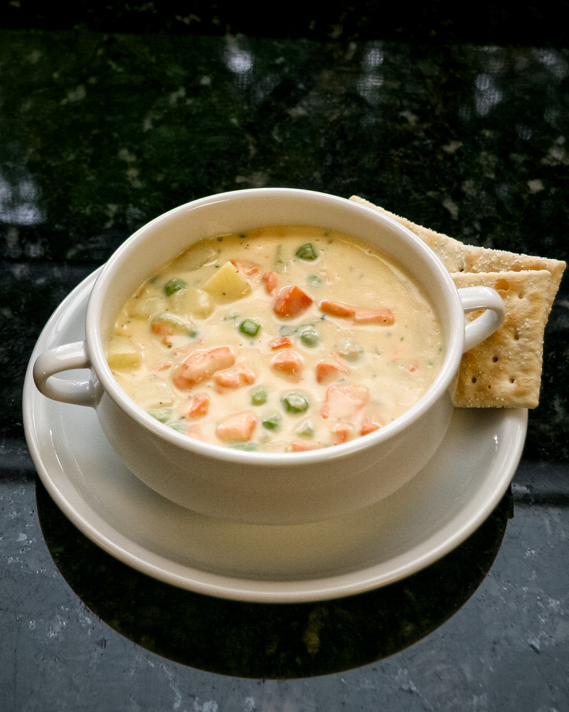 A bowl of salmon chowder with some saltine crackers on the side.