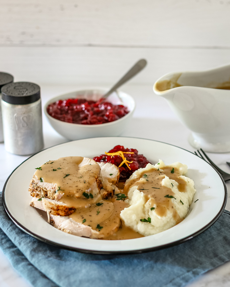 homemade gravy for turkey or chicken shown on turkey and mashed potatoes with cranberry sauce in the background.