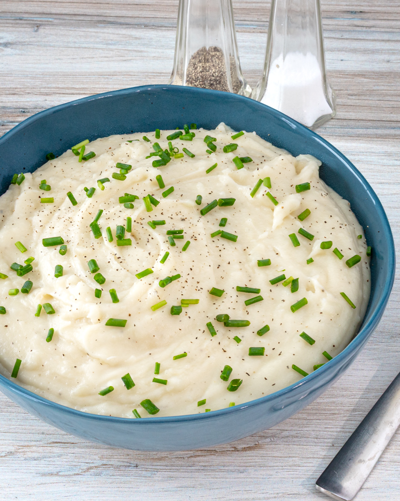 A bowl of Instant Pot pressure cooker mashed potatoes with garnish of herbs.