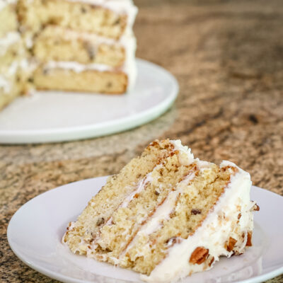 A slice of Italian cream cake on a white plate with the whole cake in the background.