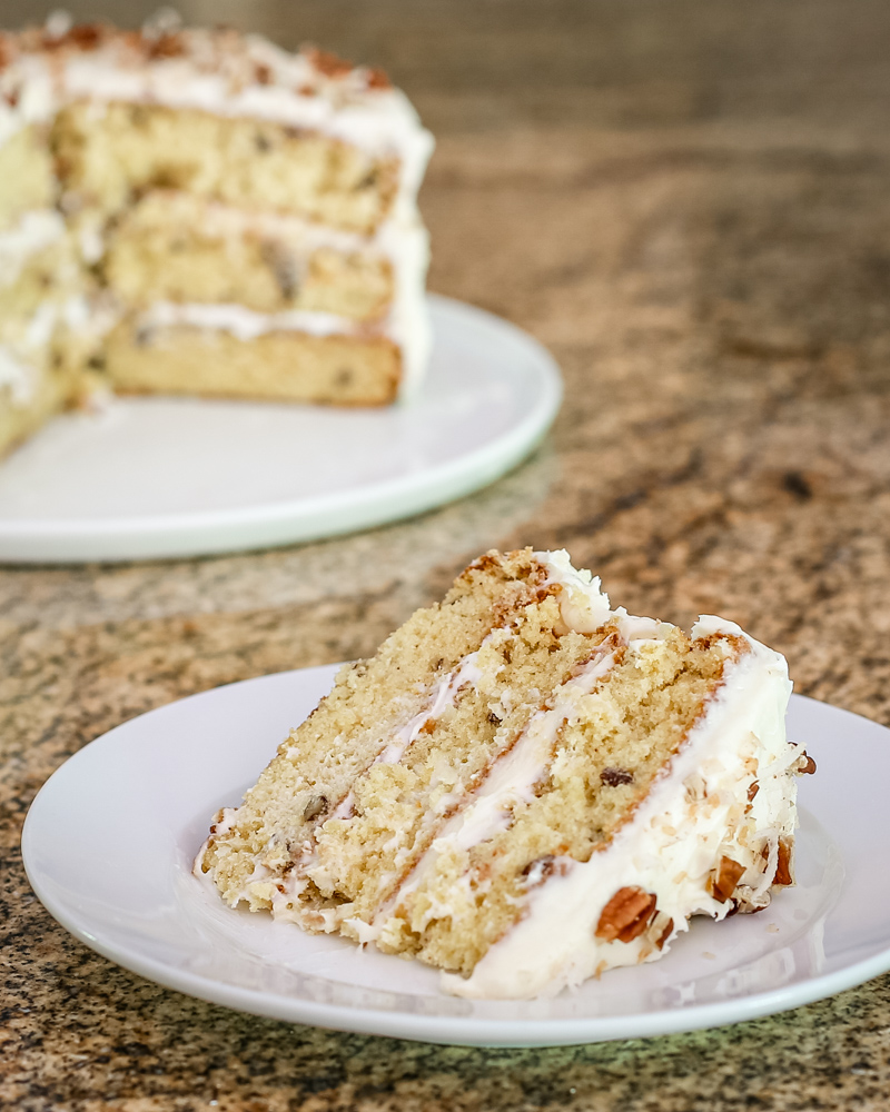 A slice of Italian cream cake on a white plate with the whole cake in the background.