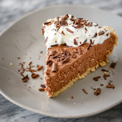 A slice of chocolate cheese cake pie with whipped cream and chocolate shavings.