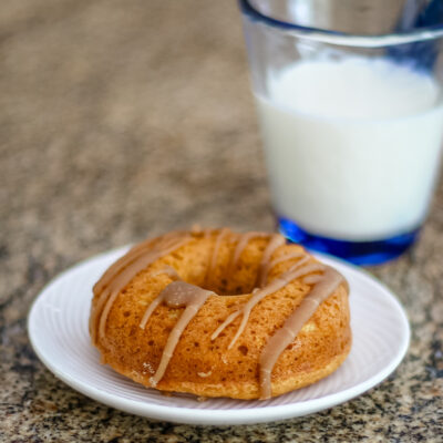 A glazed pumpkin donut on a white plate and a glass of milk.