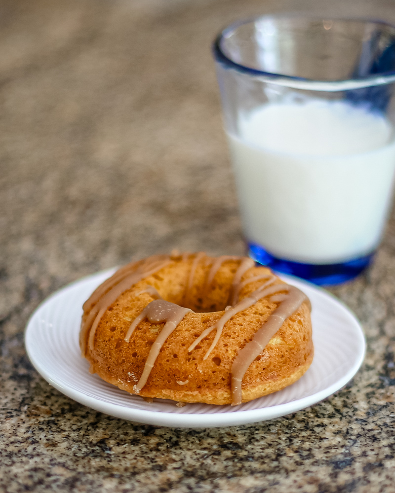 A glazed pumpkin donut on a white plate and a glass of milk.