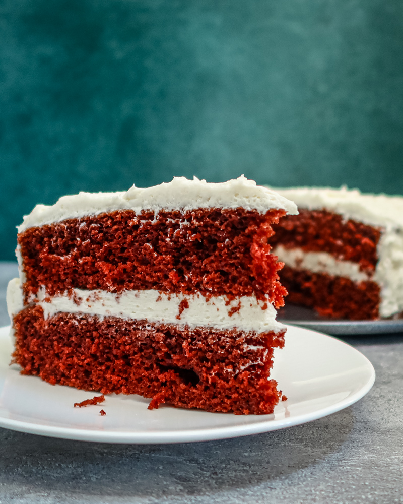 red velvet cake slice on a plate with the larger cake in the background