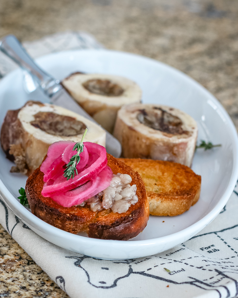 A bone marrow appetizer with crostini, thyme, and pickled red onions.
