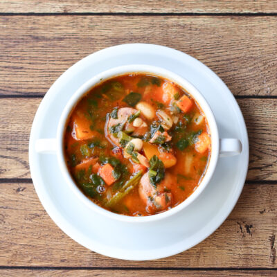 White bean soup with sausage and vegetables in a white bowl.
