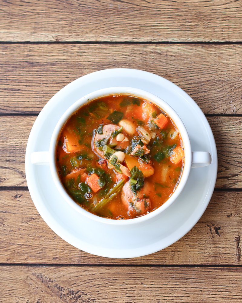 White bean soup with sausage and vegetables in a white bowl.