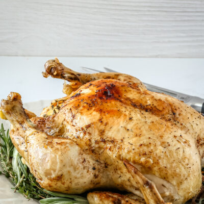 A whole roasted chicken resting on a platter lined with herbs.