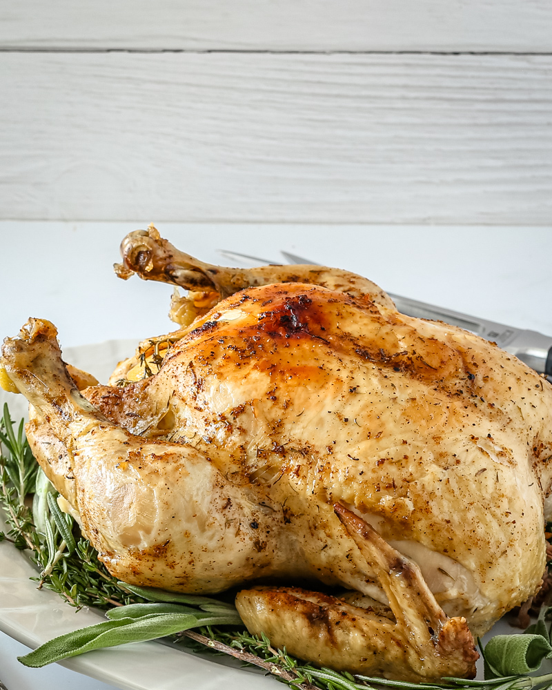 A whole roasted chicken resting on a platter lined with herbs.