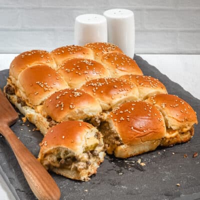 A slab of cheeseburger sliders with ground beef, pickles, a special sauce, and cheese.