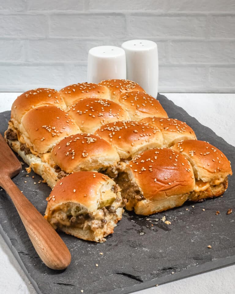 A slab of cheeseburger sliders with ground beef, pickles, a special sauce, and cheese.