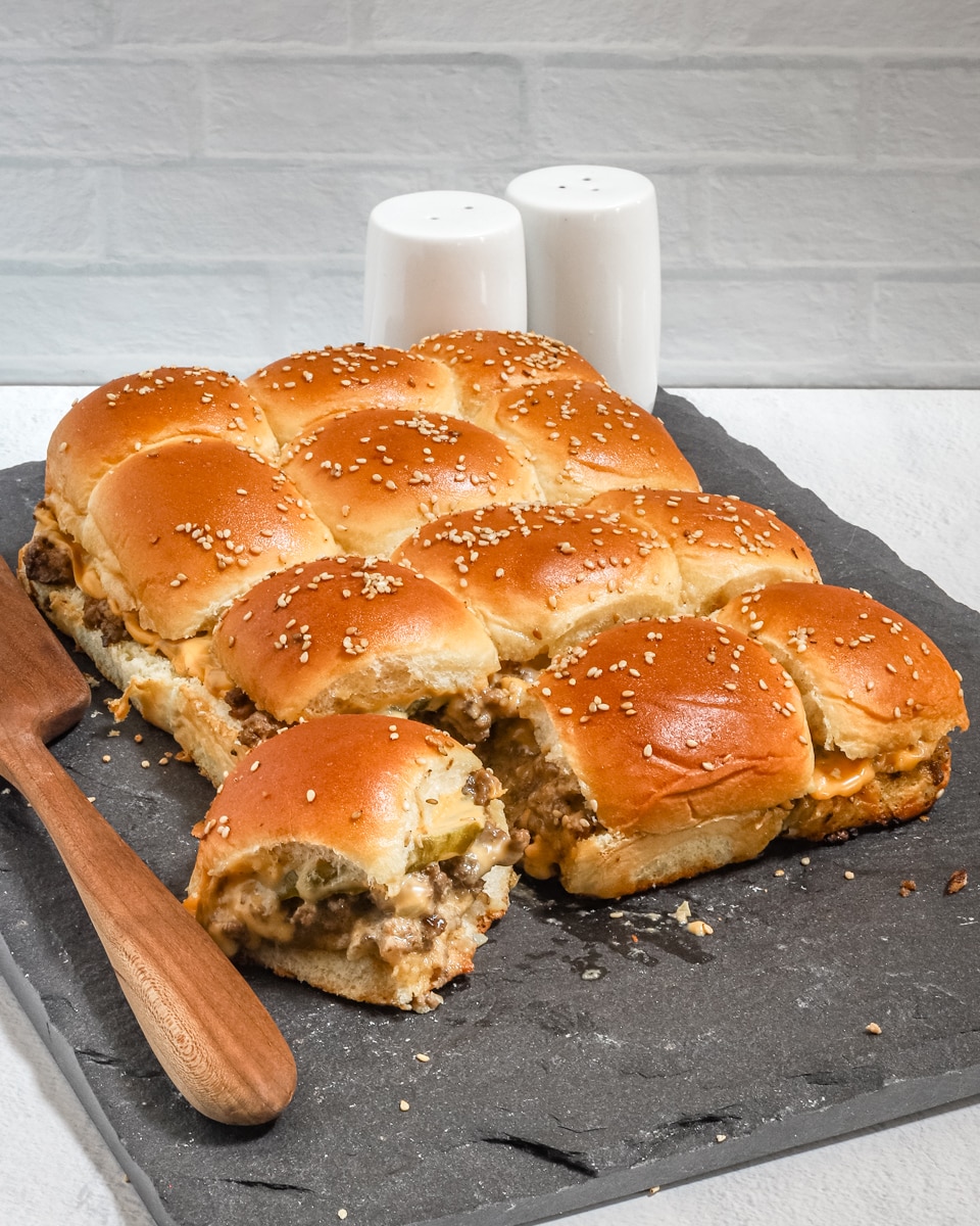 A slab of cheeseburger sliders with ground beef, pickles, a special sauce, and cheese.