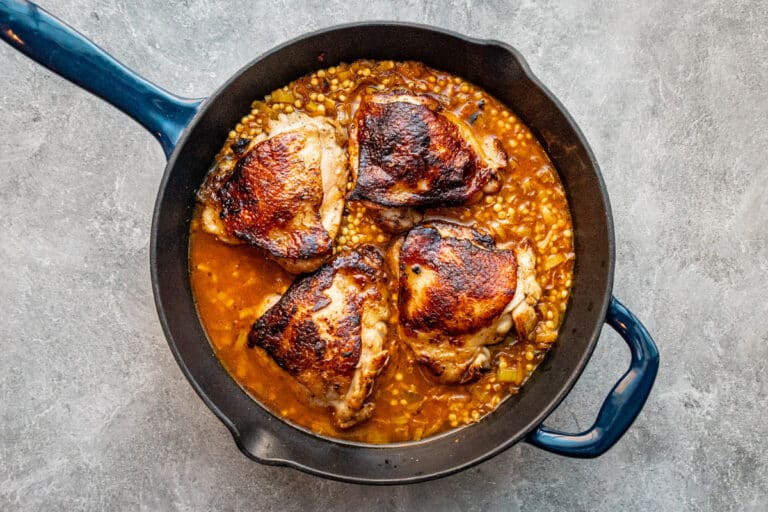 Harissa spiced chicken thighs in a skillet with couscous and a garnish of parsley.