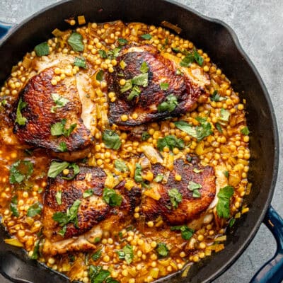 Harissa spiced chicken thighs in a skillet with couscous and a garnish of parsley.